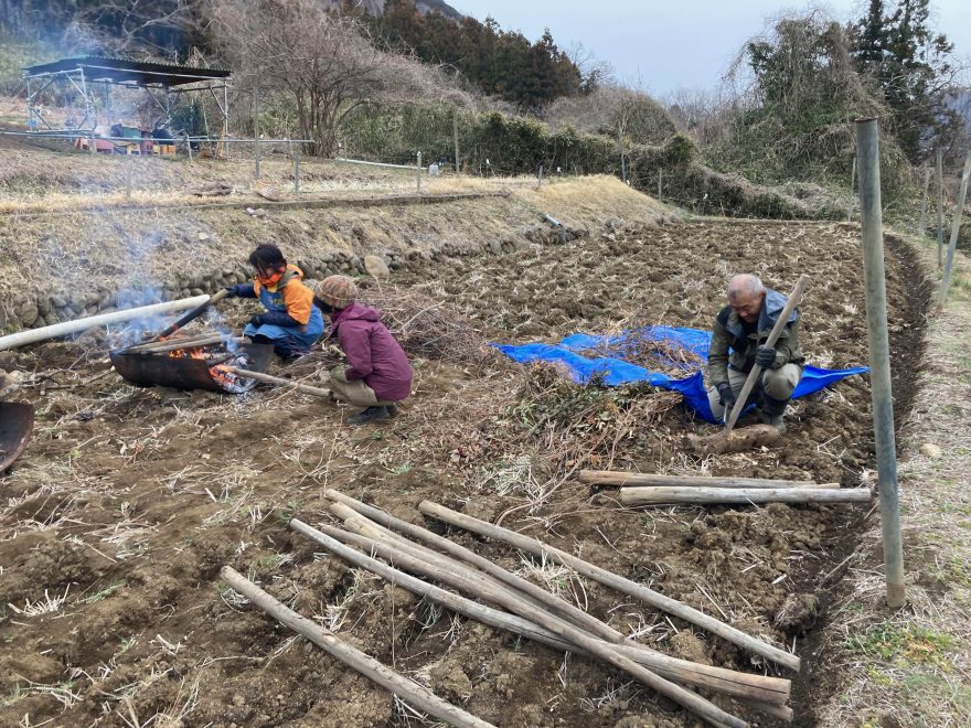 手前にある丸太杭を半分に切り、先端をナタで尖らせたあとに火で焼きます